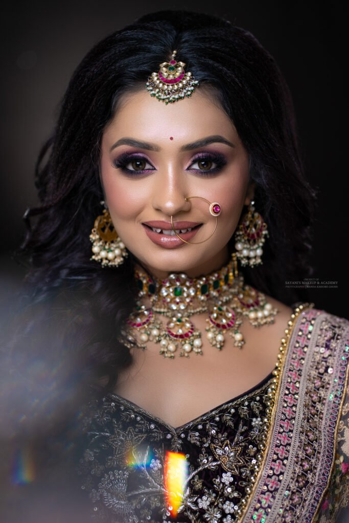 Luxury bridal beauty portrait of an Indian bride wearing a black embroidered lehenga, statement polki jewellery, and glamorous makeup with soft prism light effects.