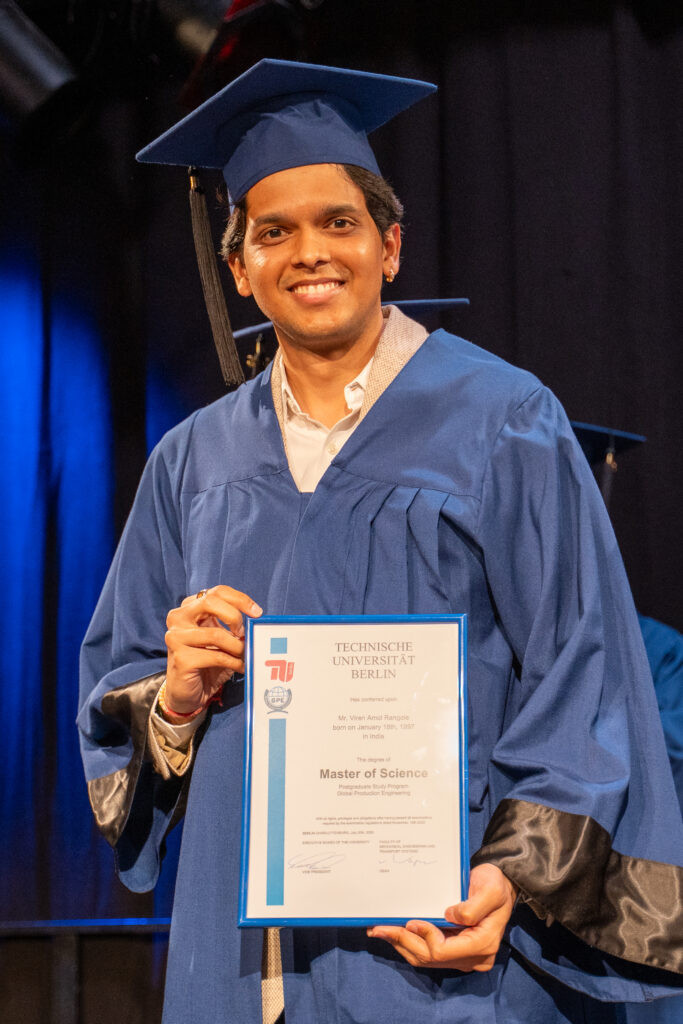 Smiling TU Berlin graduate in cap and gown holding his Master of Science certificate